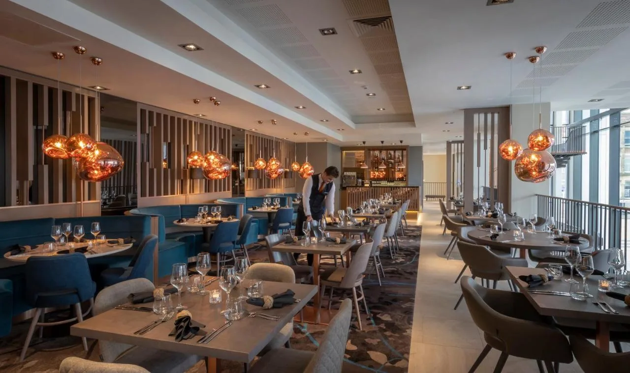 a restaurant with tables and chairs and a man standing in the middle at Clayton Hotel Manchester City Centre in Manchester
